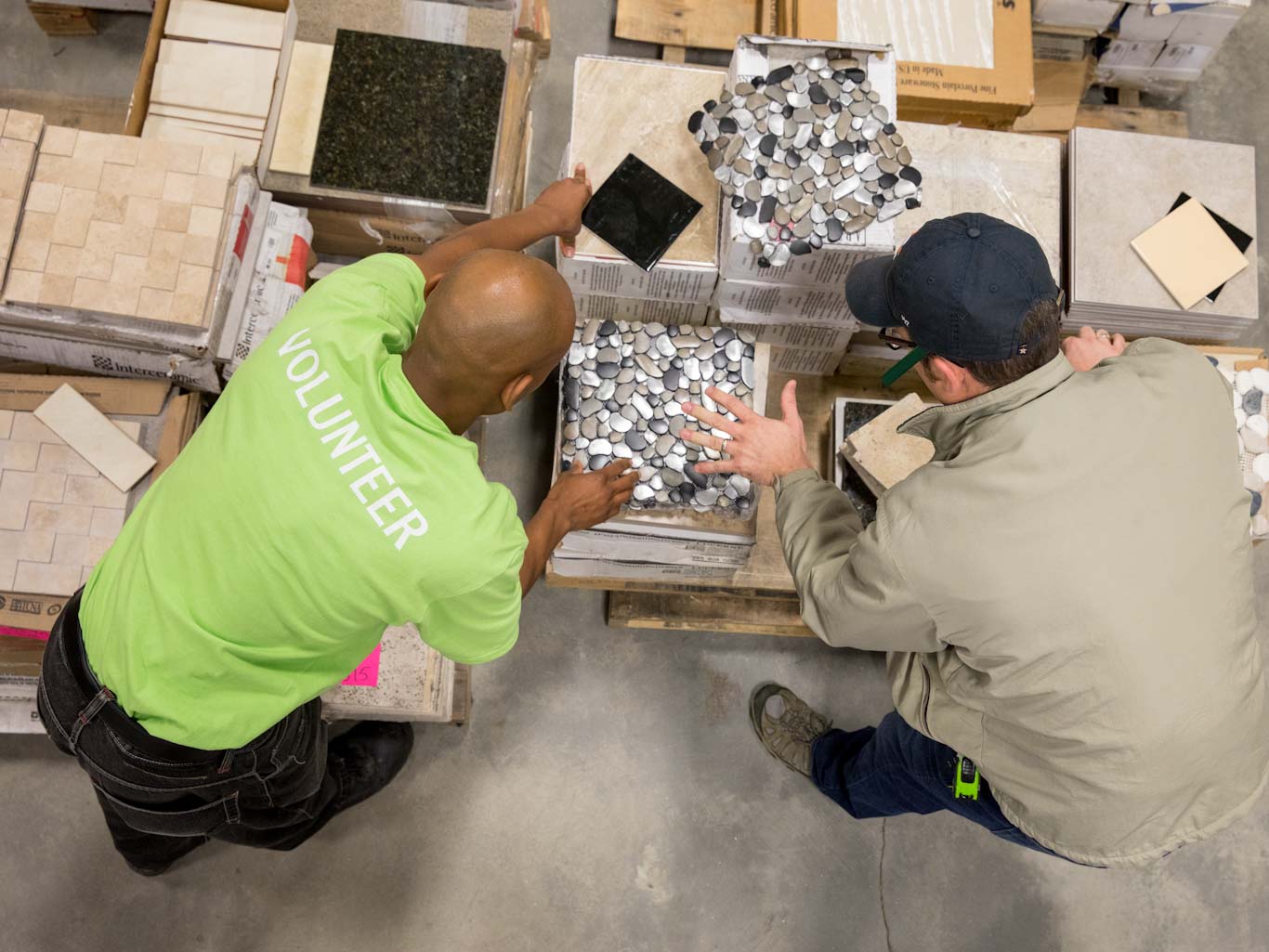 Volunteer in green "Volunteer" shirt assisting a customer with tile